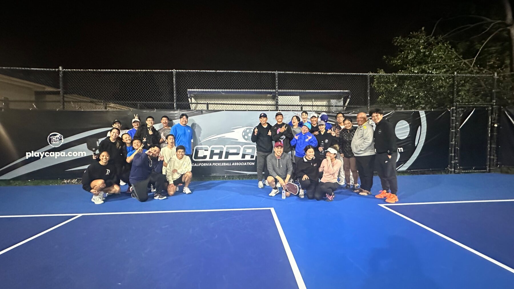 Large nighttime pickleball community gathered in front of a CAPA banner