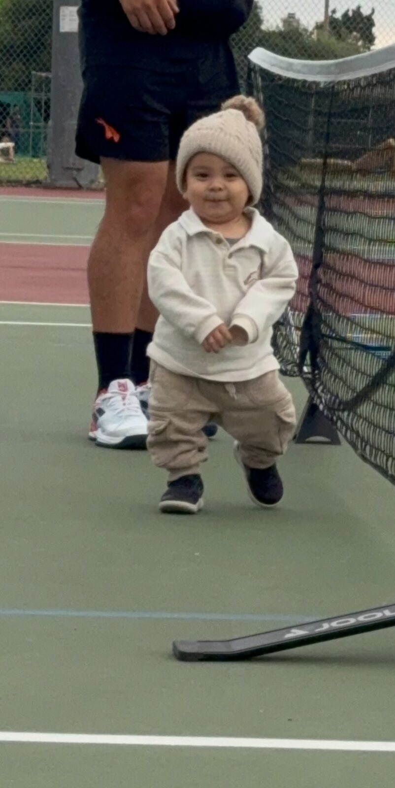 A young child walking confidently beside a pickleball net